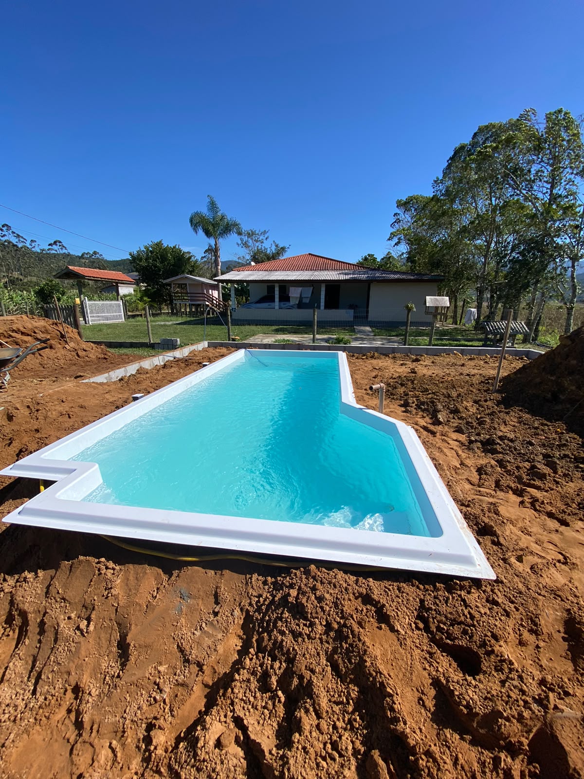 Piscina de fibra instalada e cheia de água em terreno em obra, com casa ao fundo